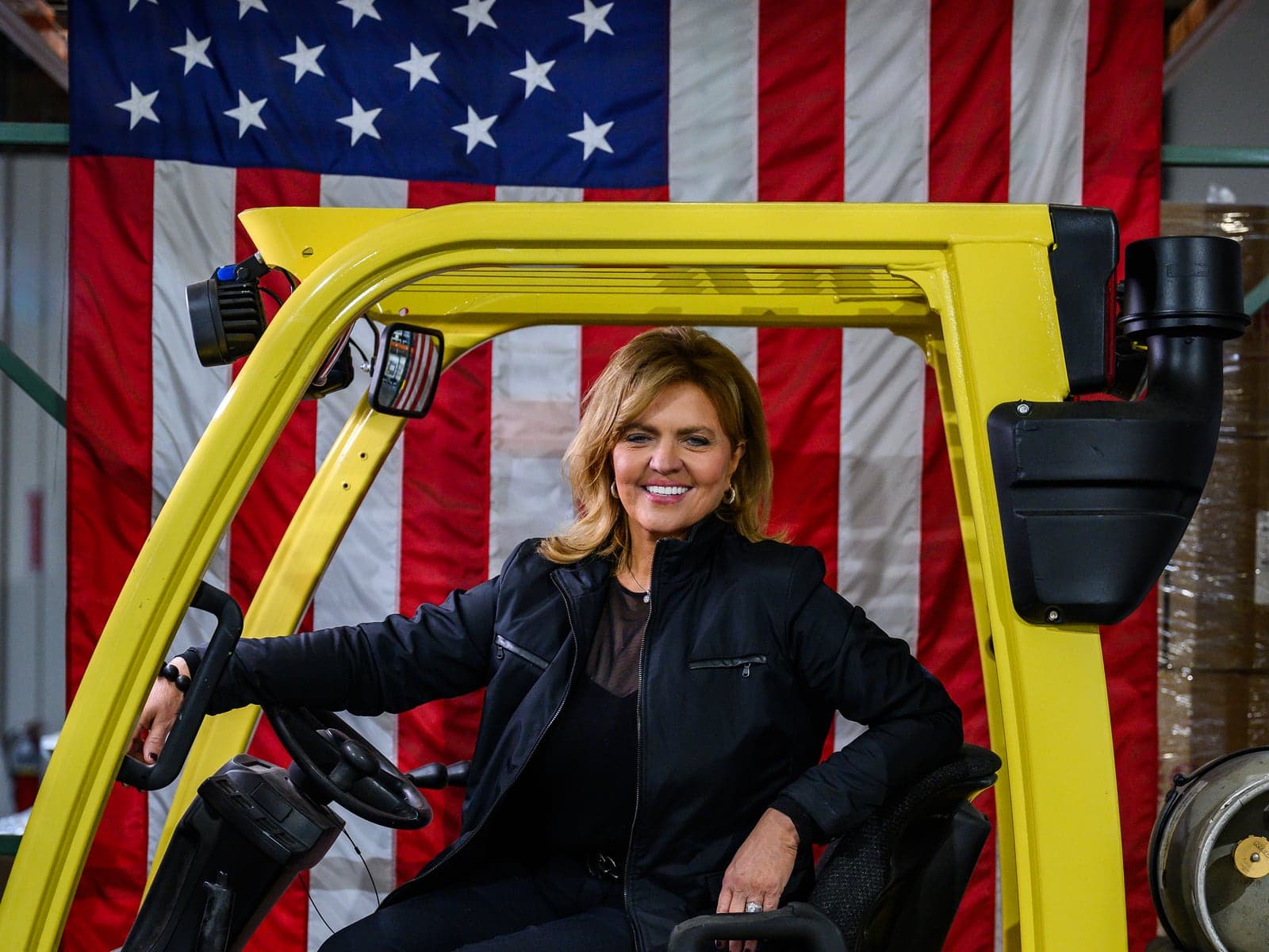 Paula Blankenship at the controls of a forklift on the Taylorsville factory floor, an American flag hanging behind her